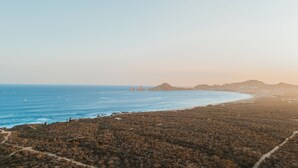 Paesaggio costiero con spiaggia, terreno roccioso e montagne in lontananza.