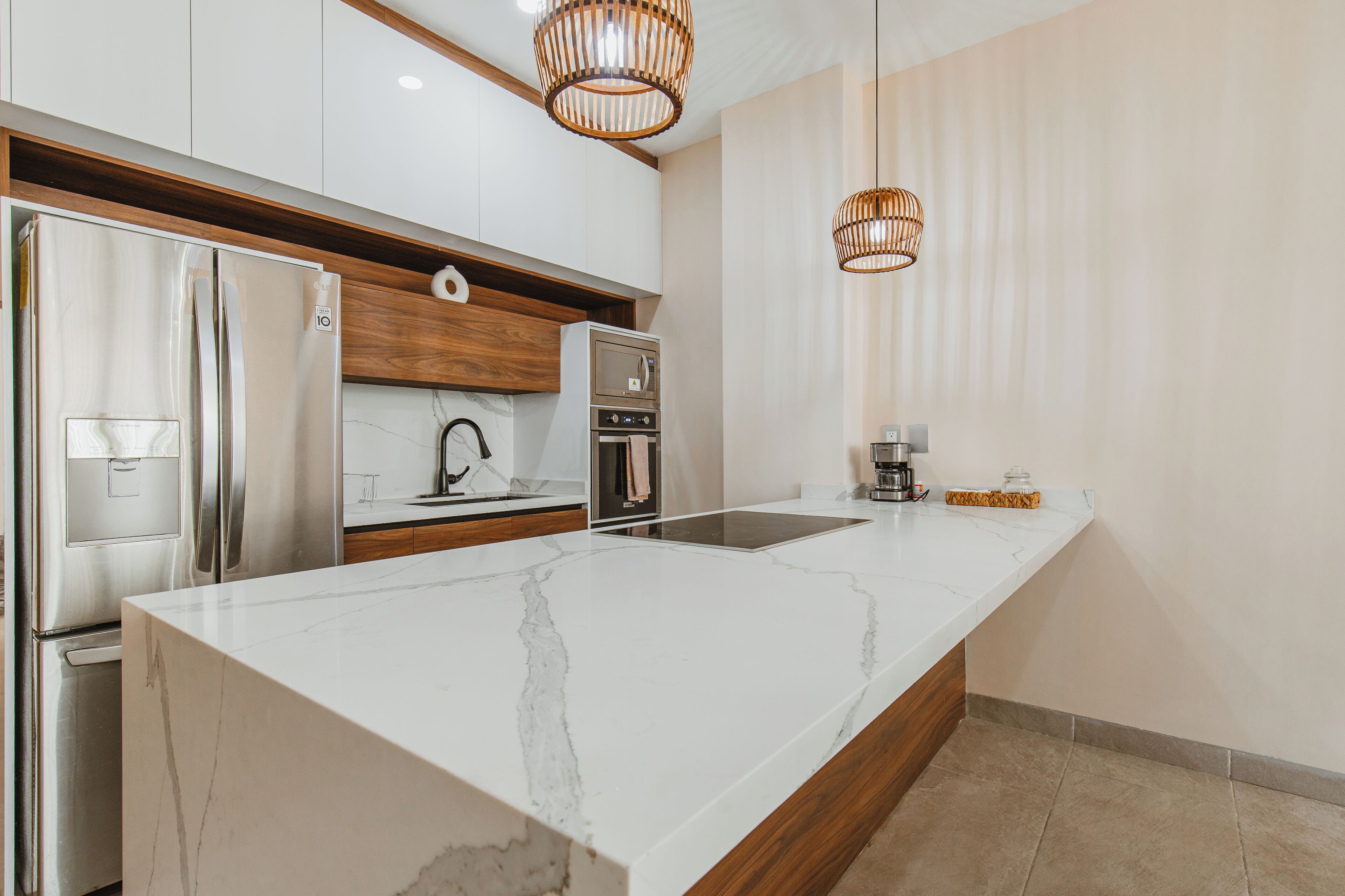 A modern kitchen with a large marble island, stainless steel appliances, wooden cabinets, and two wicker pendant lights.