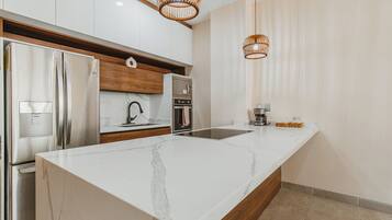A modern kitchen with a large marble island, stainless steel appliances, wooden cabinets, and two wicker pendant lights.