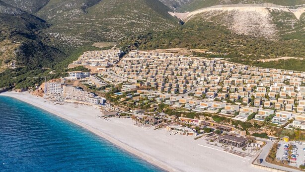 Un quartier résidentiel situé sur la côte, avec une plage et des montagnes en arrière-plan.