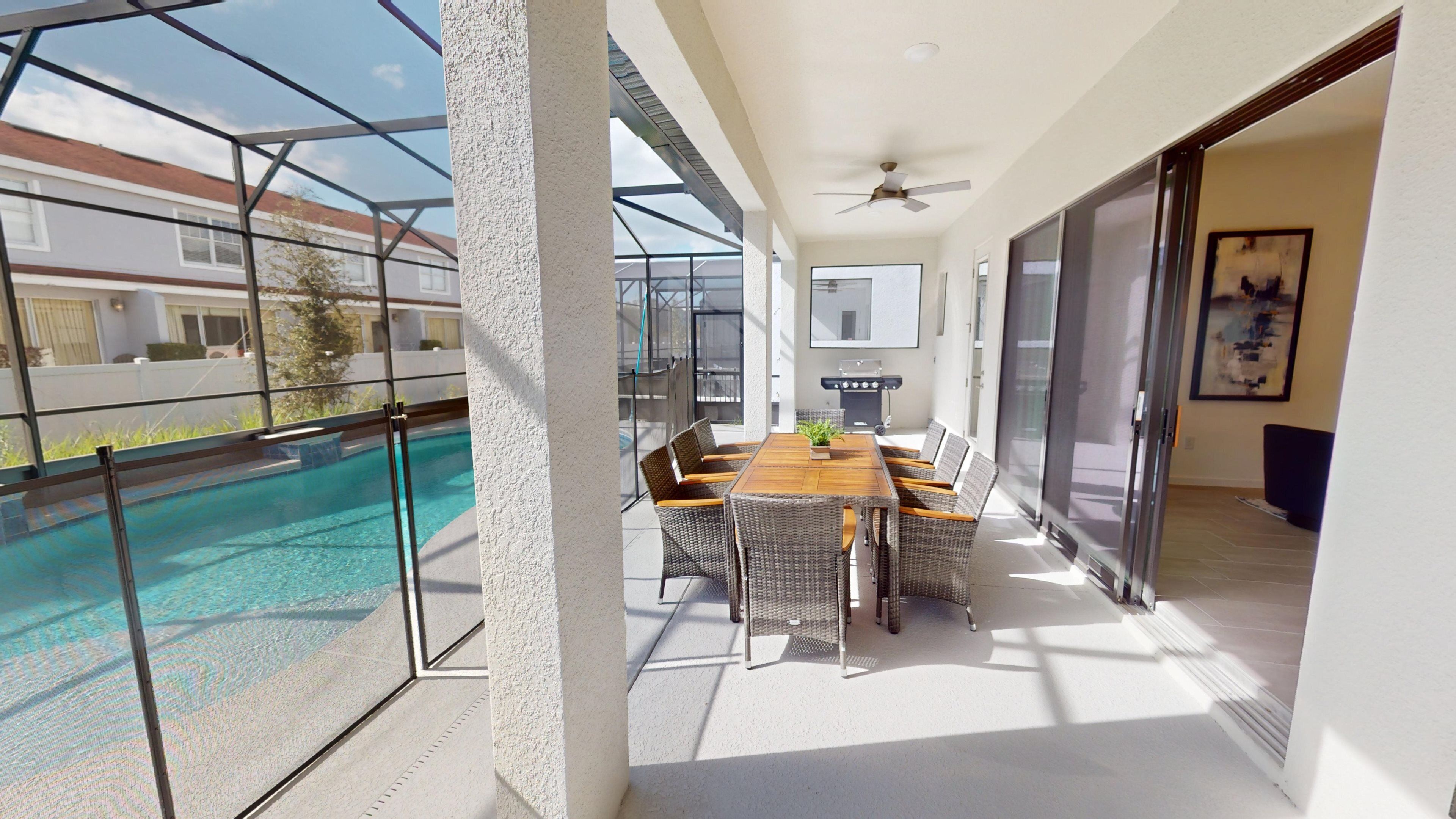 A modern outdoor patio with a pool, a dining area with wicker furniture, and a ceiling fan.