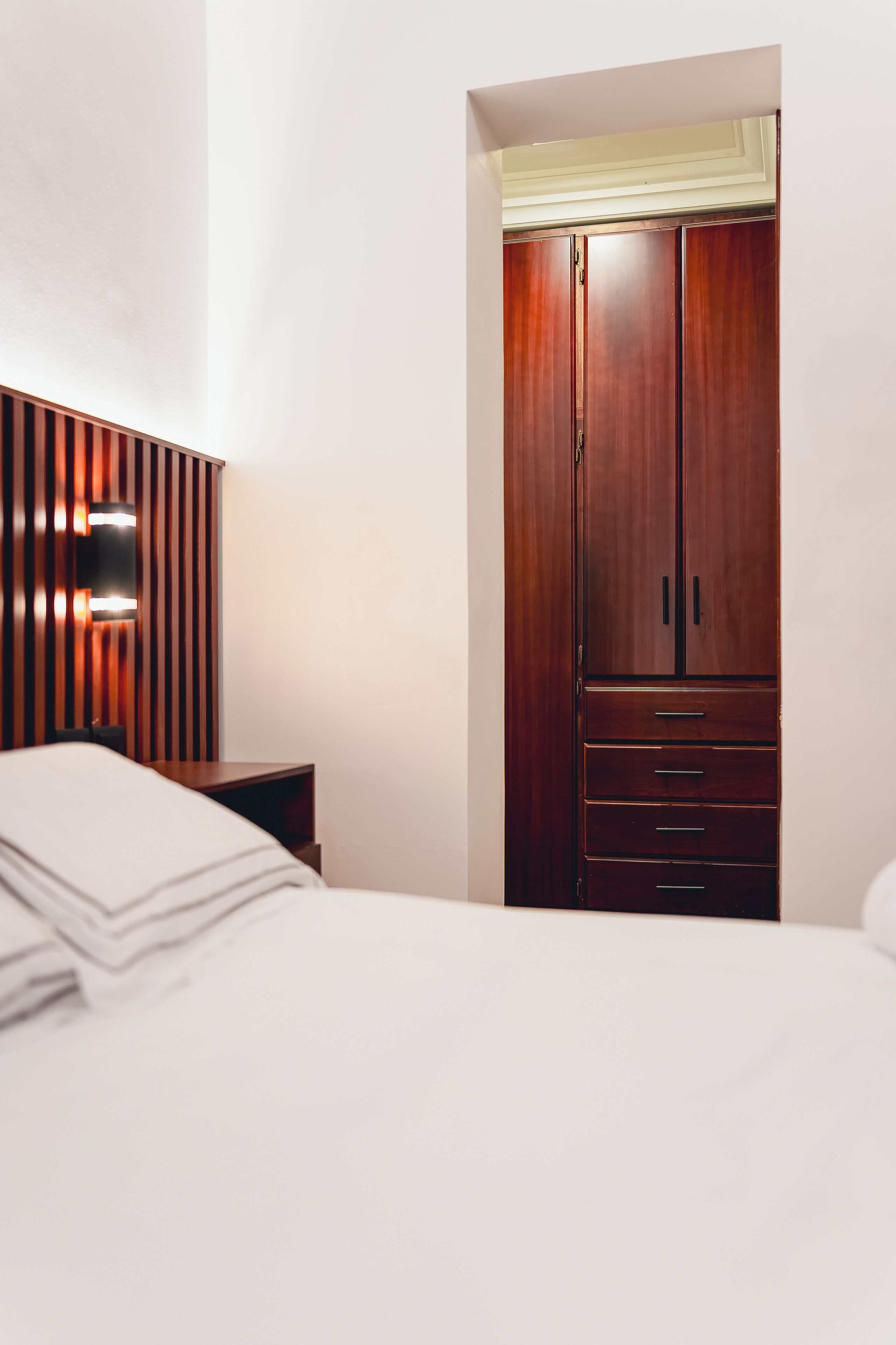 Een slaapkamer met een houten garderobe, een nachtkastje en een wandlamp.