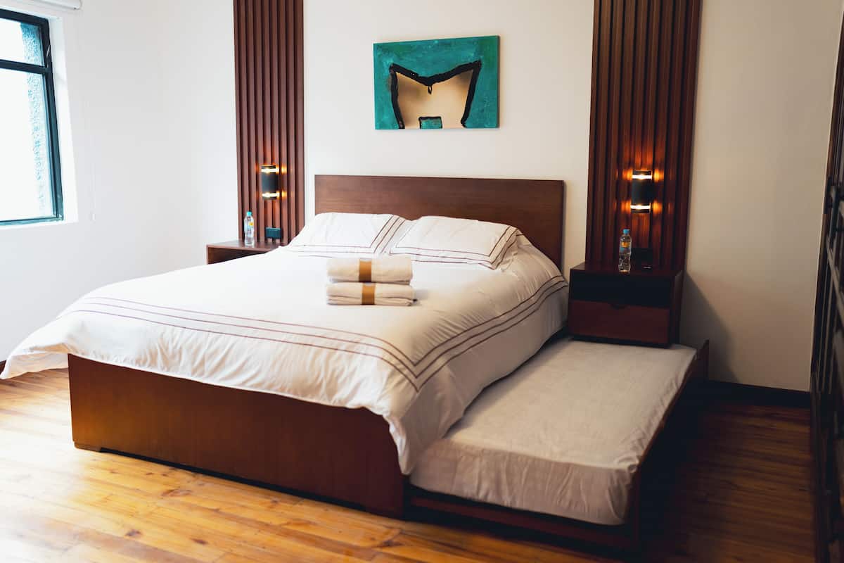 A neatly made bed with a wooden headboard, a bedside table with a bottle, and a wall-mounted artwork.