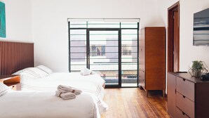 Een hotelkamer met een groot bed, een houten dressoir, een kledingkast en een glazen schuifdeur die leidt naar een balkon.