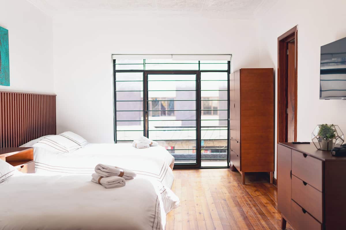 A hotel room with a large bed, a wooden dresser, a wardrobe, and a sliding glass door leading to an outdoor balcony.