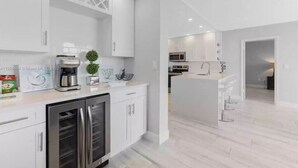 Una cucina moderna con mobili bianchi, elettrodomestici in acciaio inossidabile e un'isola integrata con posti a sedere.