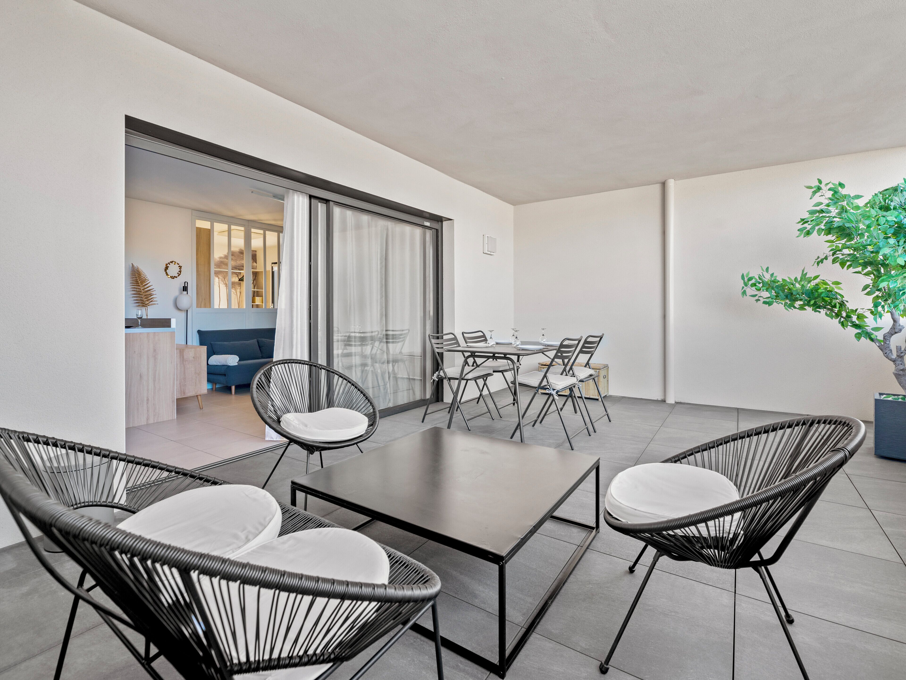 A modern outdoor dining area with a table and chairs, a blue sofa, and a potted plant.