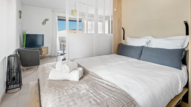 Ein modernes Hotelzimmer mit einem großen Bett, einem Fernseher, einem Schreibtisch und Blick ins Freie.
