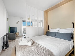 Habitación de hotel moderna con una cama grande, televisión, escritorio y vistas al exterior.