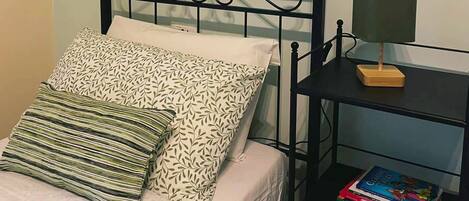 A neatly made bed with patterned pillows, a bedside table with a lamp, and a stack of books.