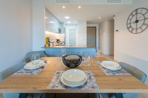 A dining area with a wooden table set for four, a black woven bowl, and a wall-mounted clock. - Apartamento Flamenca Village (Orihuela Costa)