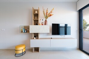 A modern living room with a flat-screen TV, a white console table, and a yellow ottoman. - Apartamento Flamenca Village (Orihuela Costa)