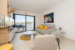 A modern living room with a grey sofa, yellow pillows, a coffee table, and a large window with a view of the city. - Apartamento Flamenca Village (Orihuela Costa)