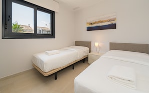 A hotel room with two beds, a window, a painting, and a nightstand with a lamp.