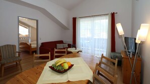 Ett rum med ett matbord dukat med frukt, en röd soffa, en tr ästol, en tv och en lampa.