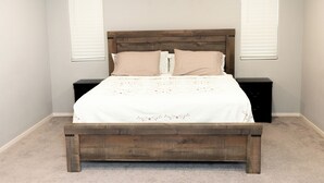 Una camera da letto con un letto a struttura in legno, biancheria da letto bianca, due comodini e un pavimento tappezzato.