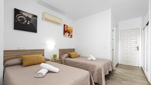 Habitación de hotel con dos camas, cabecero de madera, aire acondicionado montado en la pared y una puerta con cerradura.