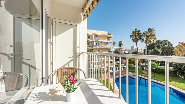 Un balcón con vista a una piscina, una silla de mimbre y una planta en maceta.