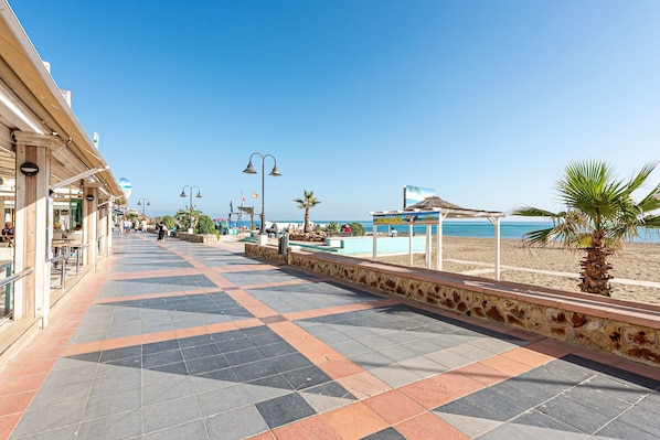 Un vialetto lastricato con un muro in pietra, una palma e una spiaggia sullo sfondo.