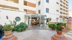 Entrada de hotel con puerta de cristal, plantas en macetas y un camino de ladrillo que lleva a la entrada.