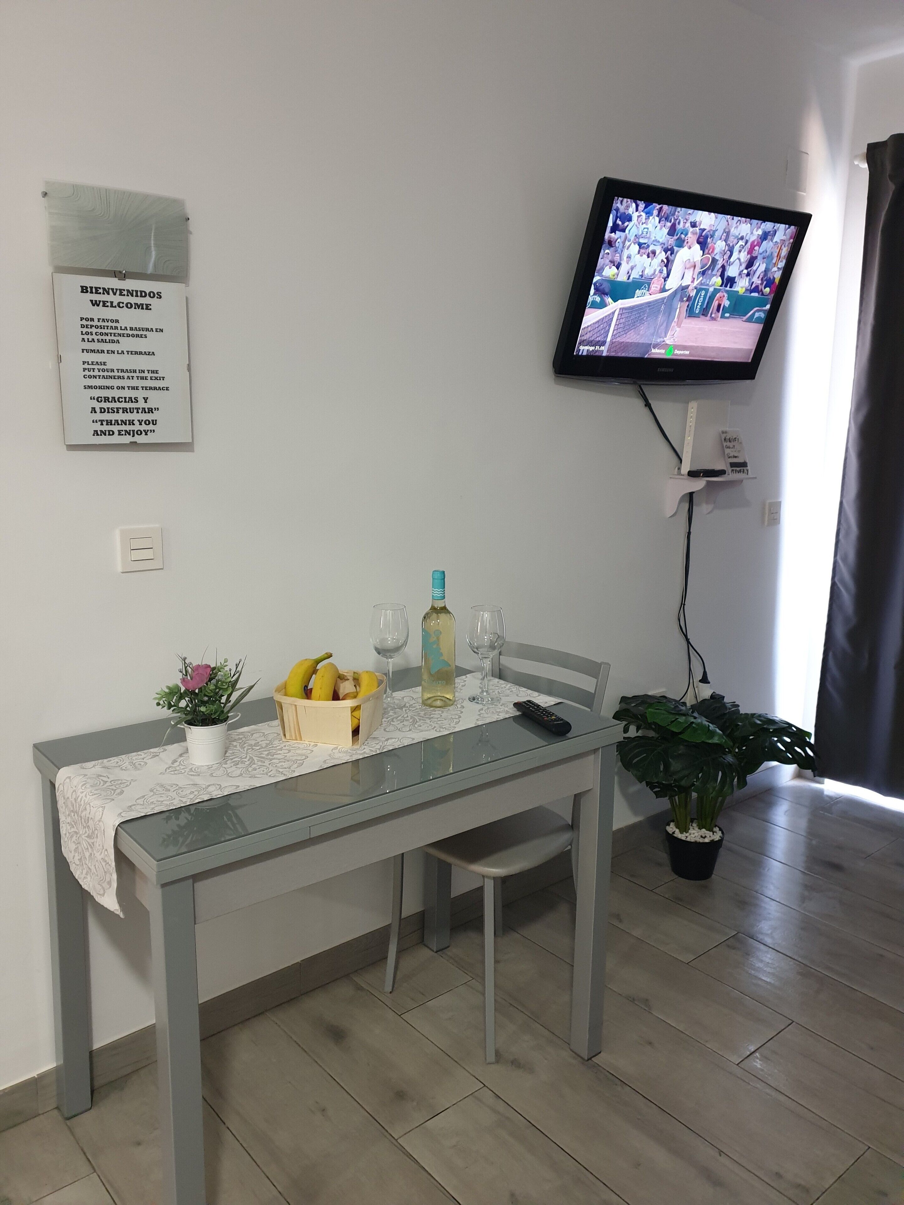 A dining area with a table set for two, a television mounted on the wall, and a sign with instructions in Spanish.