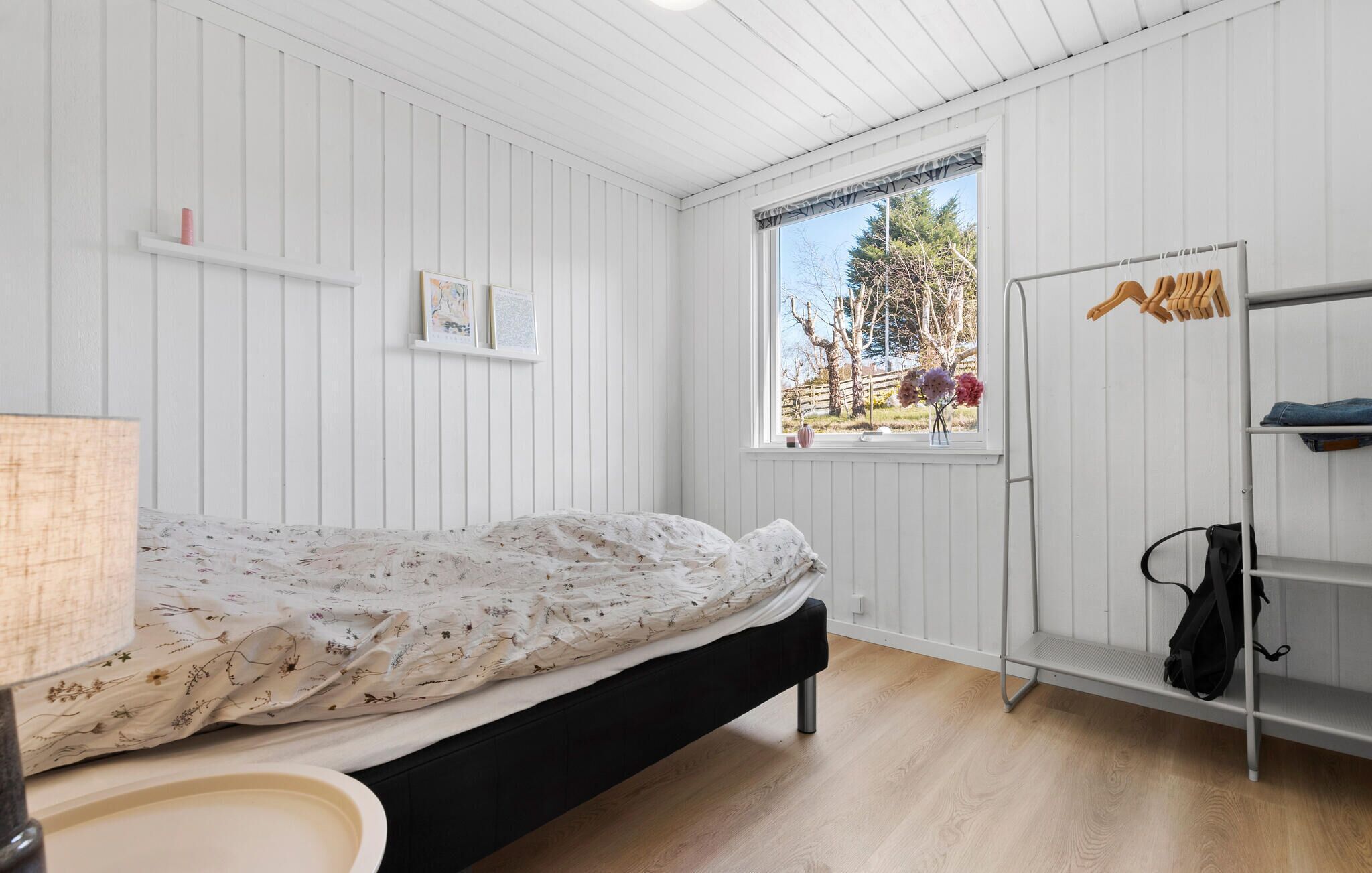 Een slaapkamer met een bed, een raam met uitzicht op bomen en een kledingrek.