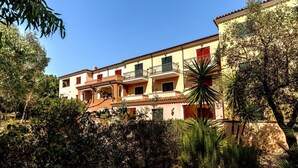 Un edificio de varios pisos con balcones, rodeado de un follaje denso y árboles.