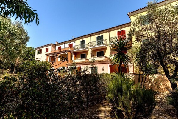 A multi-story building with balconies, surrounded by dense shrubbery and trees.