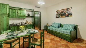 Una cocina acogedora con armarios verdes, una mesa de comedor preparada para cuatro personas y un sofá verde con cojines estampados.
