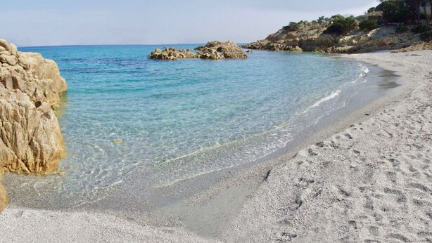 Una playa con agua turquesa cristalina, afloramientos rocosos y una orilla arenosa.