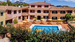 Un edificio de varios pisos con piscina, mobiliario exterior y montañas al fondo.
