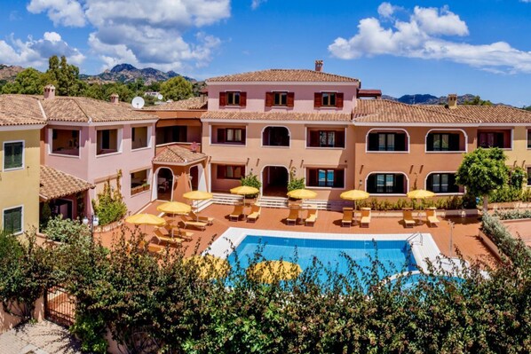 A multi-story building with a swimming pool, outdoor seating, and a mountainous backdrop.