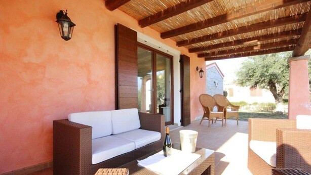 Patio esterno con mobili in vimini, un divano bianco e un tavolo con una bottiglia e una candela.
