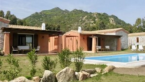 Una casa in pietra a due piani con piscina, circondata da un giardino con rocce e piante.
