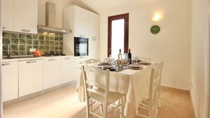 Una cucina con mobili bianchi, una parete rivestita di piastrelle, un fornello e un tavolo da pranzo per due persone.