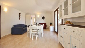 Zona pranzo con tavolo e sedie bianche, divano blu e cucina con mobili bianchi.