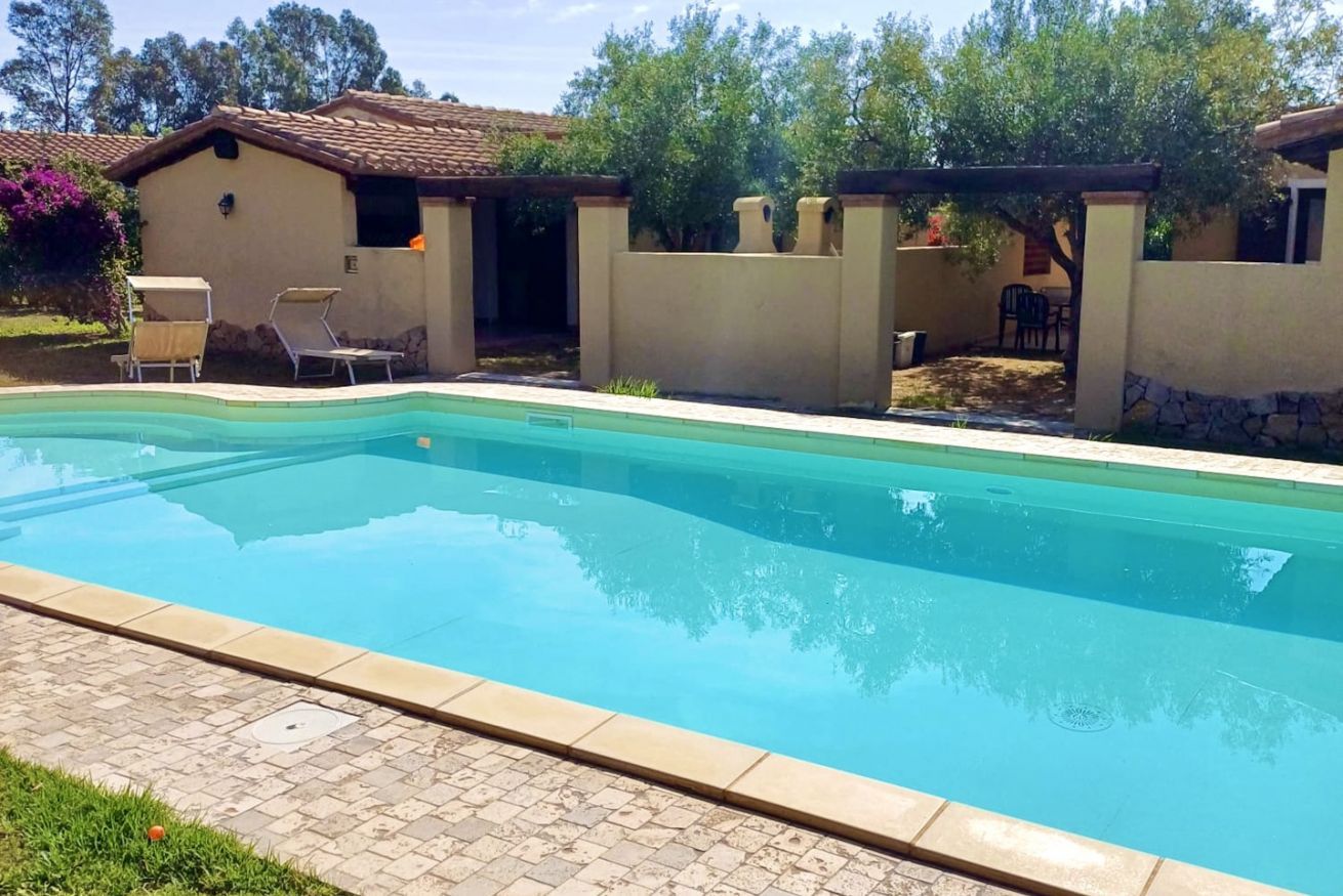 A swimming pool with a tiled deck, a covered patio area, and a small building with a tiled roof.