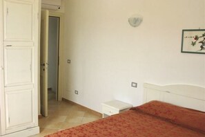 A room with a bed, a small bedside table, a wardrobe, and a door leading to another room.