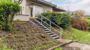 Una casa moderna con una scala che conduce a un ingresso, immersa nel verde e con un tetto spiovente.