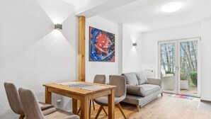 Un soggiorno moderno con un tavolo da pranzo in legno, sedie rivestite in grigio, un divano grigio e un quadro astratto colorato appeso alla parete.