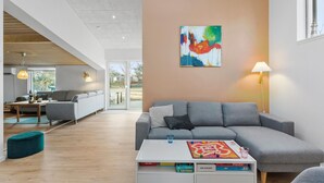 A modern living room with a grey sofa, a coffee table with books, and a colorful abstract painting on the wall. - 4 bedroom awesome home in Storvorde (Storvorde)