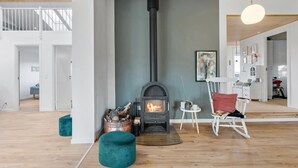 A modern living room with a wood-burning stove, teal ottomans, and a white rocking chair. - 4 bedroom awesome home in Storvorde (Storvorde)