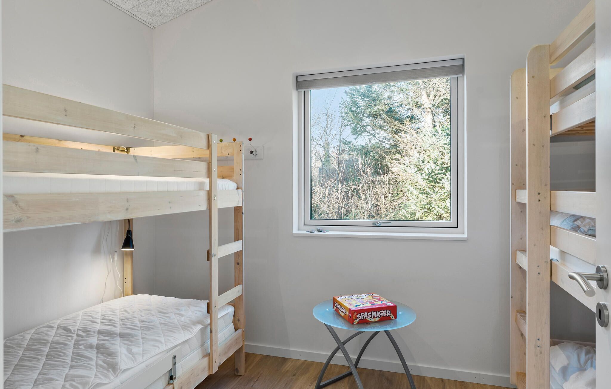 A child's bedroom with bunk beds, a window with a view of trees, and a small table with a box on it.