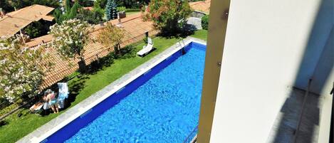 Una piscina con una vista despejada de los alrededores, incluyendo un edificio con tejado de azulejos y una masa de agua al fondo.