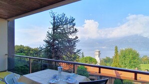 A balcony with a table set for two, overlooking a scenic view of a lake and a tower.