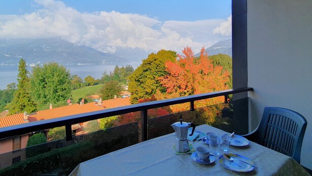 A balcony with a table set for breakfast, overlooking a scenic view of a lake and mountains. - Apartment in Luino With Lake Maggiore Views (Luino)