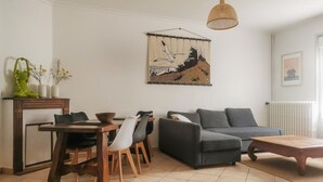 Un soggiorno con tavolo da pranzo, sedie, un divano grigio, tavolino da caffè, lampadario e un'ampia opera d'arte incorniciata appesa al muro.