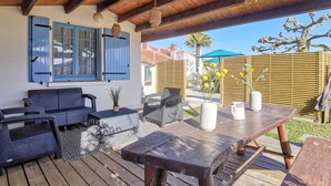 Una veranda esterna con mobili in vimini, un tavolo di legno e una porta blu con persiane.