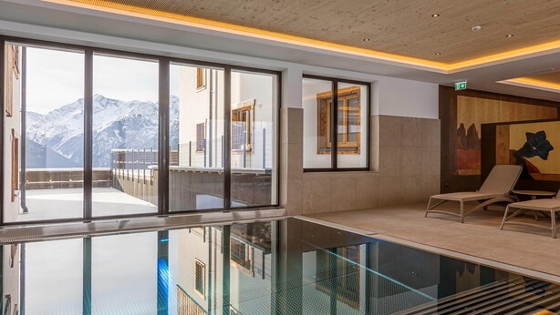 A modern indoor pool area with large windows offering mountain views, a lounge area with chairs, and a wooden ceiling. - Studio Near the Slopes With Wellness Area (Mittersill)