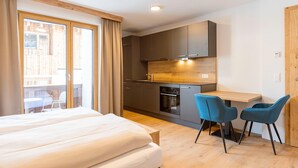 A modern hotel room with a bed, a small kitchenette, two chairs, and a large window. - Studio Near the Slopes With Wellness Area (Mittersill)